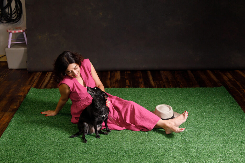 Reference photograph of Michelle sitting on artificial turf in the studio while her dog Miya looks up at her, used as the basis for the fantasy painting.